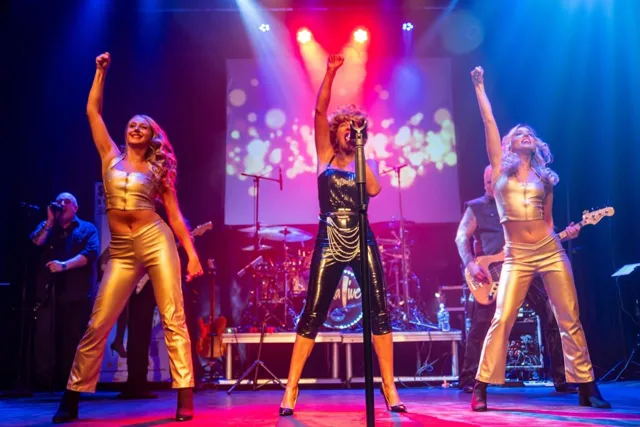 Julie and two dancers in gold costumes raising their arms