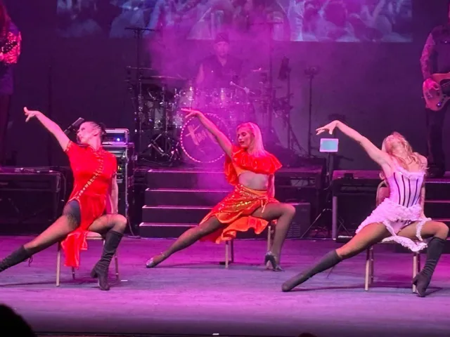 Three dancers performing a chair routine under pink stage lights