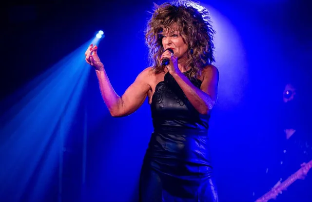 Julie performing in a black dress under vivid blue lighting